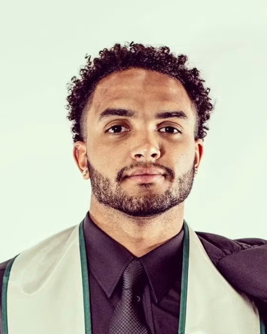 Portrait of Cameron Dollar in a dark shirt and tie with his Charlotte 49ers graduation stole.
