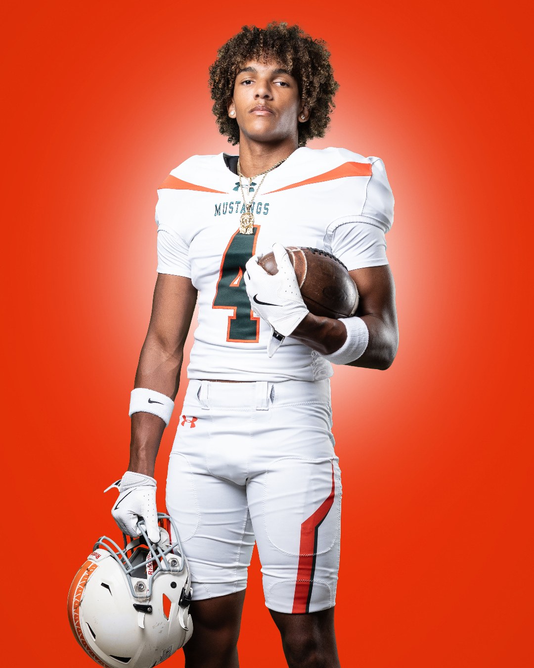 Studio portrait of Jaxon Dollar in his white East Lincoln Mustangs number 4 uniform, holding a football and his helmet.